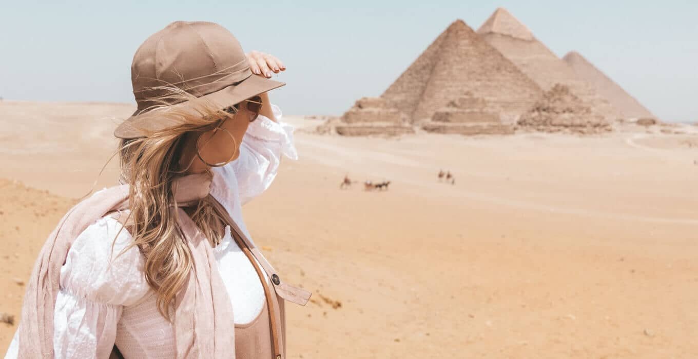 Traveler girl in sun hat looking at the Giza Pyramids of Egypt