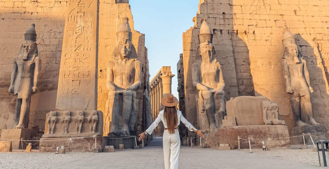 Traveler woman in hat posing in front of Luxor Temple colossi