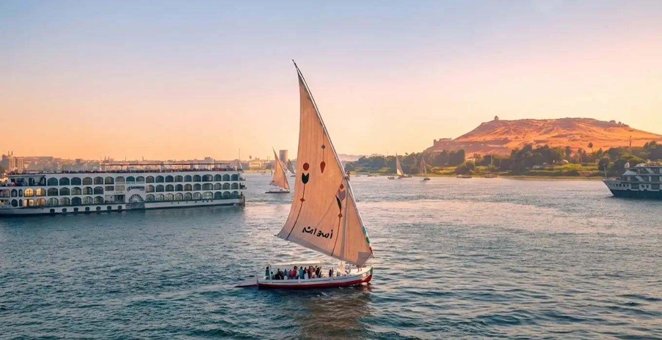 Traditional felucca boat trips on the Nile River with a Nile cruise ship and desert hills in the background.